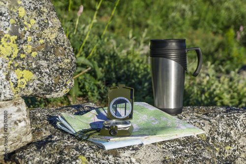 Fotografija a breather in the way - a map, a compass and a thermo cup on a stone on a natura