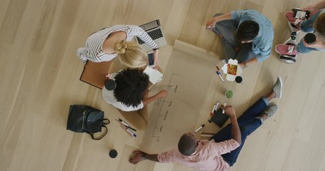 young diverse group of web developers brainstorming ideas for startup business website drawing on paper planning design layout wooden floor top view