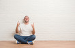 © Krakenimages.com - Young caucasian man sitting on the floor over white brick wall shouting with crazy expression doing rock symbol with hands up. Music star. Heavy concept.