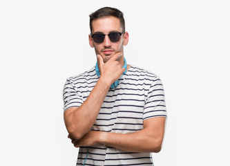 Sticker - Handsome young man wearing headphones looking confident at the camera with smile with crossed arms and hand raised on chin. Thinking positive.