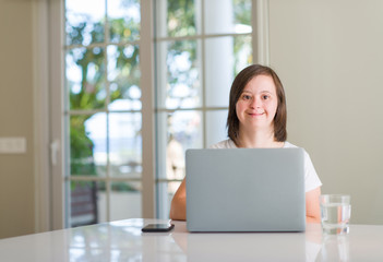 down syndrome woman at home using computer laptop with a happy face standing and smiling with a conf