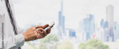 Business man using smart phone on window office with city building background and copy space.