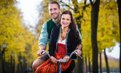 Wall Mural - Man and woman in southern German Tracht riding bicycle together laughing