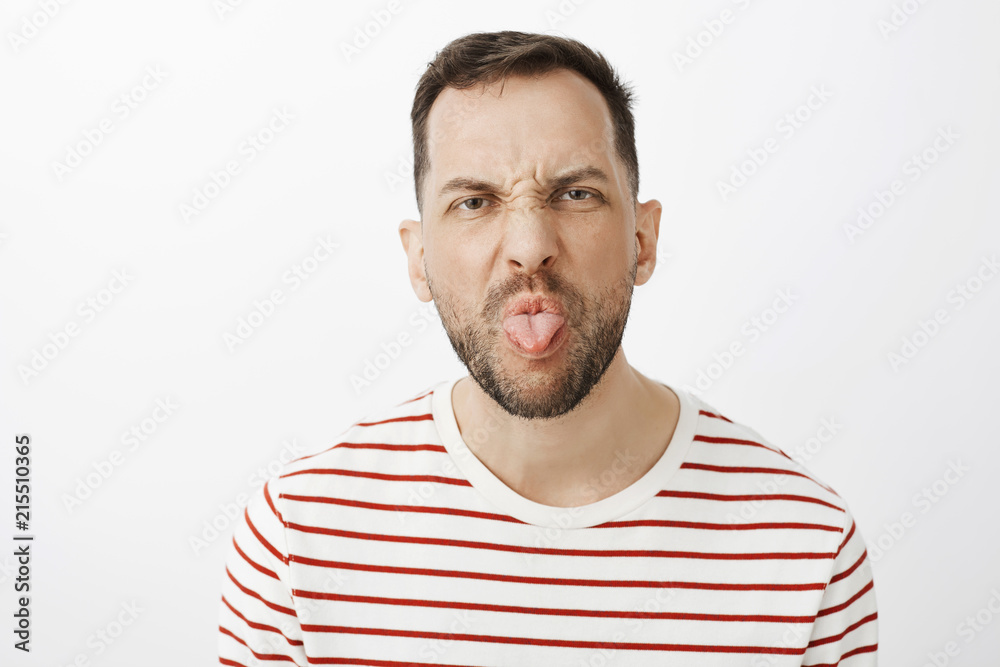 Hate doing house chores. Portrait of displeased disobedient husband with bristle, frowning and sticking out tongue while being rude and having argument with child, being childish and impolite - obrazy, fototapety, plakaty 