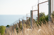 State Border Razor Barbed Wire And Fence Along Sea Shore And Forest