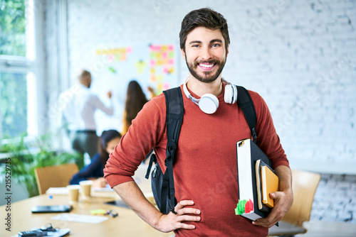 Cuadros en Lienzo Portrait of male student standing with books in classroom and looking at camera