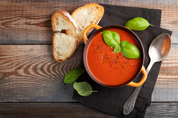 Homemade tomato soup with Basil, toast and olive oil on a wooden table. Prepared a vegetarian dish on a dark background. Top view with copy space