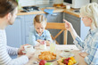 © pressmaster - Upset little girl sitting by served table while mother telling her not to eat dessert before meals