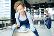 © pressmaster - Young woman in workwear painting rotating clay jug in blue color while sitting by pottery wheel in workshop