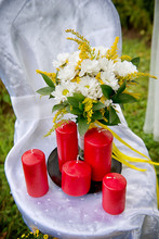 A Bouquet Of Daisies Near To Red Wax Candles On A White Chair.