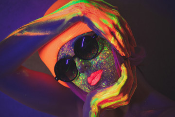 Young girl in hat with fluorescent paint on lips and face and sunglasses. Studio shot.