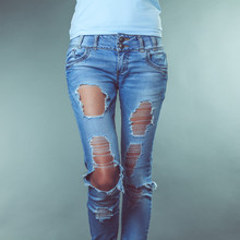 Female legs in torn jeans on a gray background