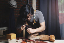Asian Carpenter Working In Woodworking Workshop. Carving Wooden Horse Sculpture