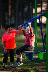 Wall Mural - Elderly woman on the sport playground doing exercises on the simulator with the coach.