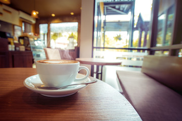 White cup of hot coffee on table in cafe with morning light , vintage  retro color toned.