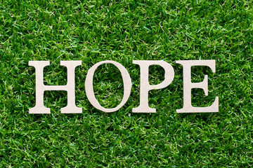 Wood alphabet in word hope on artificial green grass background