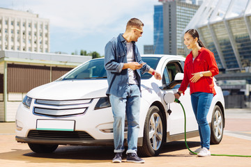 Wall Mural - Pleasant interaction. Happy nice woman talking to her male friend while fuelling the car