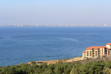 view from above on a green forest, blue sea and small yellow houses