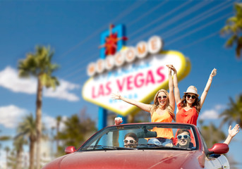 Wall Mural - summer holidays, road trip and travel concept - happy friends driving in convertible car and waving hands over welcome to fabulous las vegas sign background