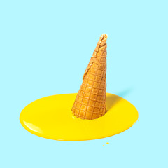 Wall Mural - Melted yellow fruit ice cream in a waffle horn on a light blue background. Summer mood. Creative concept.