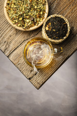 Wall Mural - top view steamed glass cup of tea with herbal on wooden table