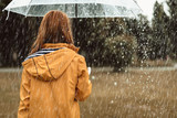 Fototapeta  - Autumn solitude. Woman standing with back turned and holding umbrella outdoors. She is strolling on her own enjoying wet weather. Copy space in right side