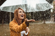 Waist up portrait of smiling girl standing outdoors with umbrella in hands. She is stretching hand and opening mouth in true pleasure