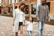 © Yakobchuk Olena - Full length of smiling mother and father walking on street with child. Small girl is holding their hands while looking at mom with joy