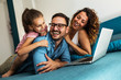 © BalanceFormCreative - Happy family lying on bed and watching something on laptop. Laughing and having fun.