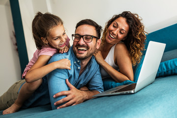 Happy family lying on bed and watching something on laptop. Laughing and having fun.	