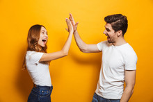 Image Of Friendly Young People Man And Woman In Basic Clothing Laughing And Giving High Five, Isolated Over Yellow Background
