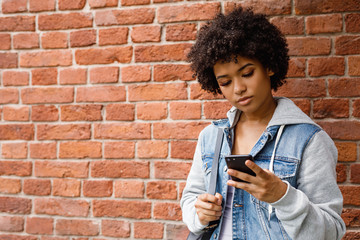 Wall Mural - Teenage girl chatting on the mobile phone. Young woman checking social media outdoors.