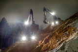 Fototapeta Miasta - The yellow excavator works at night in the headlights and additional lights. Loads of sand. Night shooting.