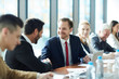 © pressmaster - Cheerful excited businessmen in formal suits celebrating success and making handshake while sitting at conference table, they attending management course