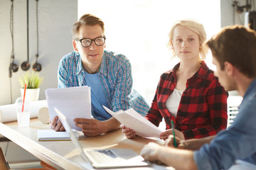 Group of creative business professionals discussing ideas while collaborating on startup project during meeting in modern office standing at table in sunlight