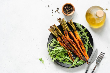 Wall Mural - Roasted carrots and fresh green vegetarian salad. Top view. Healthy vegan salad on black plate