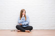 © Krakenimages.com - Young adult woman sitting on the floor in autumn over white brick wall looking confident at the camera with smile with crossed arms and hand raised on chin. Thinking positive.