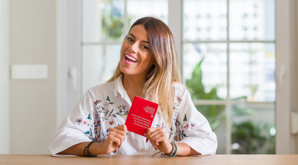 Wall Mural - Young woman at home holding a passport of Switzerland with a happy face standing and smiling with a confident smile showing teeth