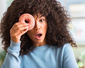 Sticker - African american woman holding donut at home scared in shock with a surprise face, afraid and excited with fear expression