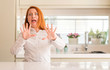 © Krakenimages.com - Redhead woman at kitchen afraid and terrified with fear expression stop gesture with hands, shouting in shock. Panic concept.
