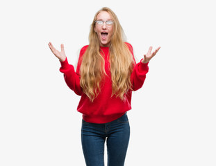 Canvas Print - Blonde teenager woman wearing red sweater crazy and mad shouting and yelling with aggressive expression and arms raised. Frustration concept.