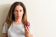 © Krakenimages.com - Middle age woman holding a green apple with a confident expression on smart face thinking serious
