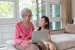 © Satjawat - Grandmother and granddaughter using laptop computer and sitting on sofa  at home