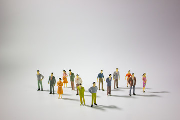 A big group of miniature business people stand on gray background.