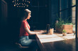 © deagreez - Young girl in a red T-shirt sitting in cafe behind a laptop and writing an article for a magazine