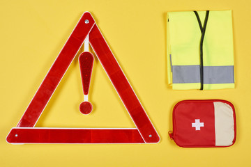 top view of warning triangle road sign, first aid kit and reflective vest isolated on yellow