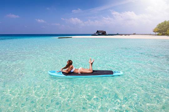 Fernweh Konzept: attraktive Frau im Bikini sonnt sich auf einem Sufbrett über den tropischen Geässern der Malediven