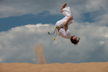 Acrobat performs an acrobatic trick, somersault on the beach.