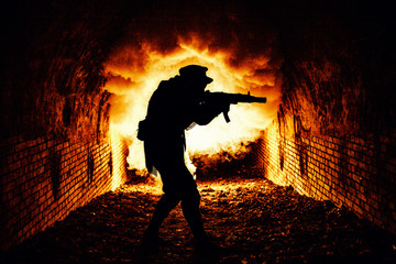 Silhouette of post apocalyptic soldier or survivor shooting with automatic firearm weapon in dark dungeon, city sewage tunnels, or underground bunker with explosion fire and smoke on background