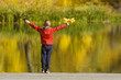 © somemeans - Boy in red jacket standing on the pier with leaves in his hand. Autumn sunny day. Back view